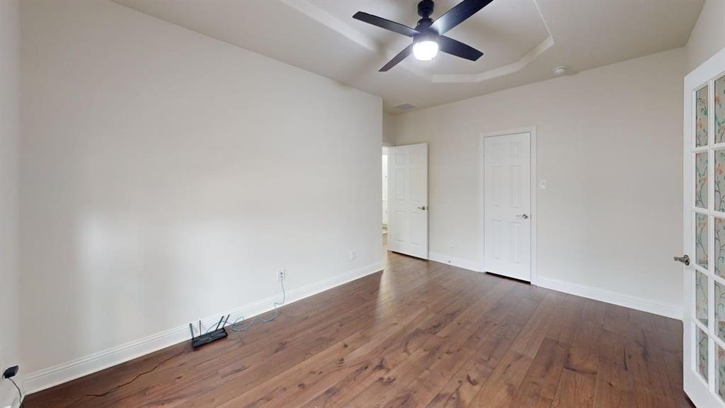 Room featuring wood-finish flooring, a tray ceiling, and a ceiling-mounted light fixture with fan