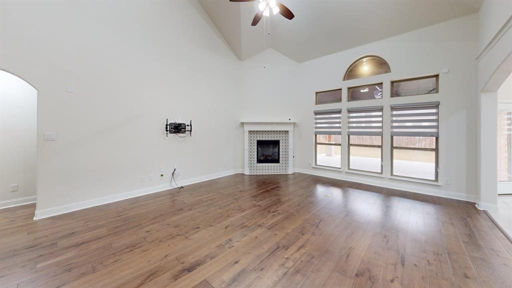 Vaulted ceilings featuring a central fan, wood-finish flooring, and a fireplace with a tiled surround