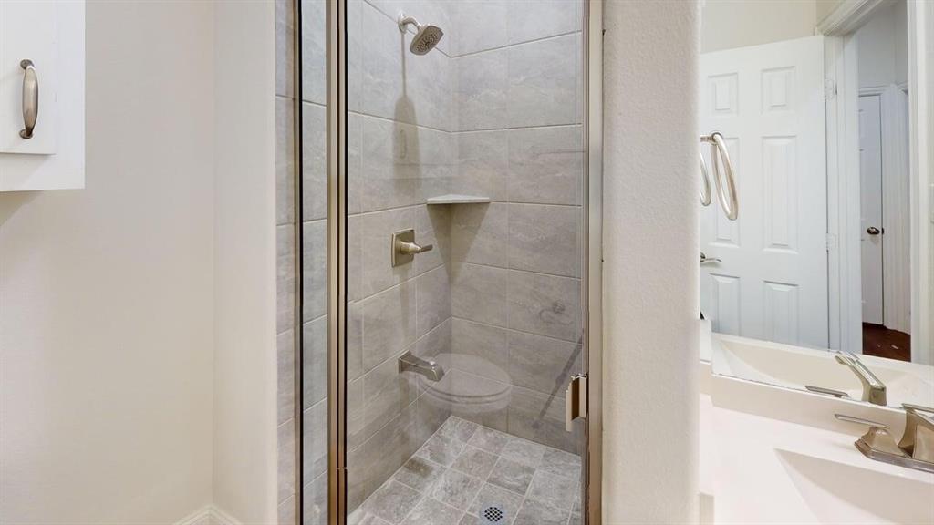 Walk-in shower enclosure with neutral-toned tiled walls, built-in corner shelf, and metallic fixtures, featuring a vanity with a solid surface countertop and undermount basin