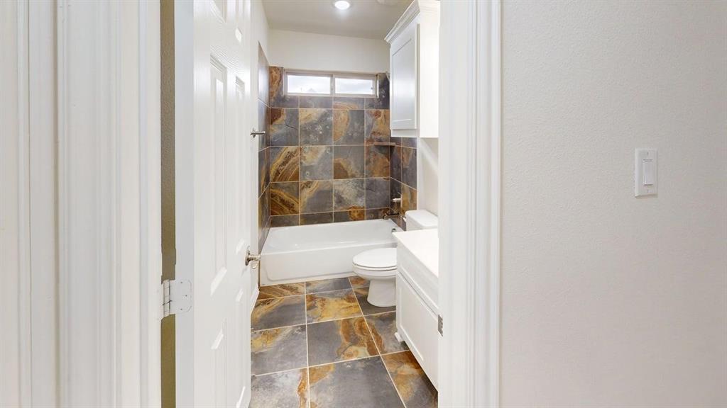 Bathroom featuring multi-tonal stone tile flooring and shower surround, white cabinetry, and a transom window