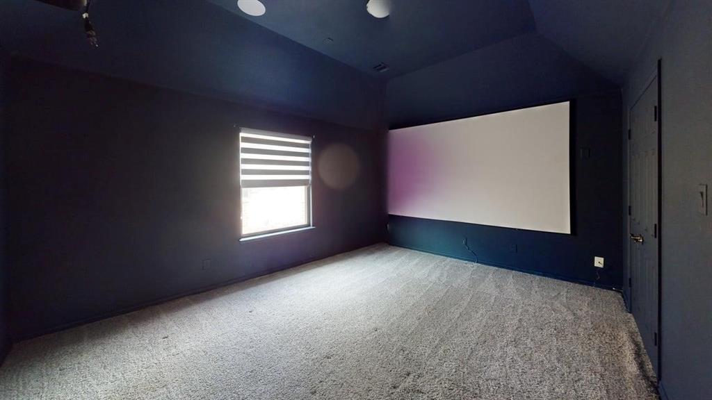 Vaulted ceiling, wall-mounted projection screen, neutral carpeting, and a single window with integrated adjustable blind