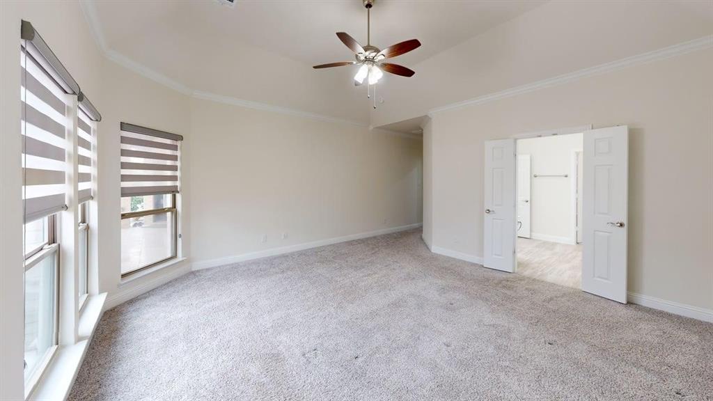 Vaulted ceiling featuring a central multi-blade ceiling fan, neutral wall-to-wall carpeting, and double doors opening to a separate room with wood-finish flooring