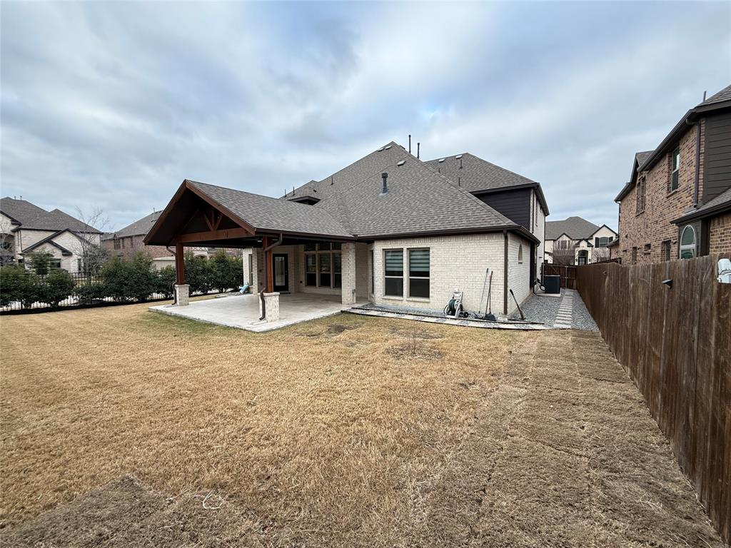 Rear exterior featuring a covered patio with timber framing, stone-clad support pillars, masonry facade, and wood-panel privacy fencing