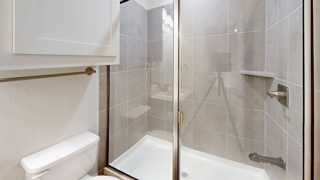 Walk-in shower featuring large-format ceramic tile surround, integrated shelving, glass enclosure with metallic trim, and wall-mounted shower fixture