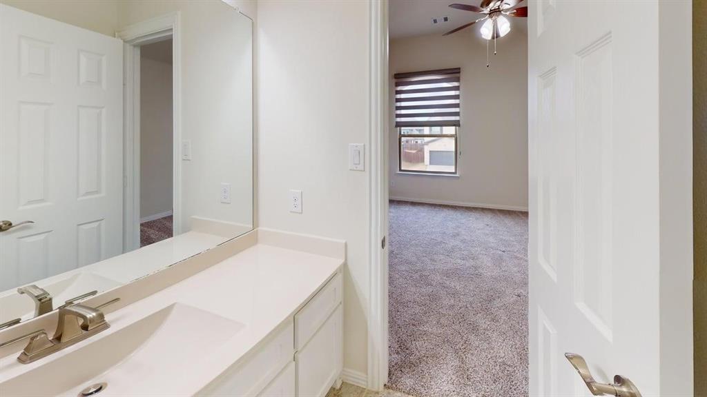Bathroom featuring a white vanity with integrated sink, polished metal faucet, large frameless mirror, and neutral wall-to-wall carpeting