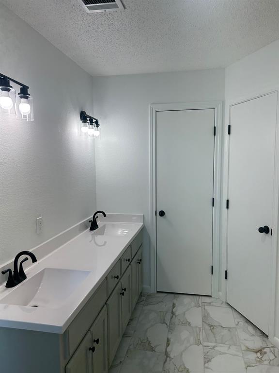Dual-vanity cabinet featuring a white solid-surface countertop with integrated sinks, matte black widespread faucets, matching matte black vanity lighting, and light-toned tile flooring