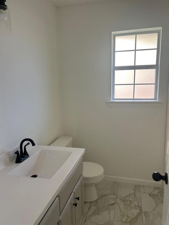 Bathroom featuring a vanity with a white countertop, rectangular integrated sink, and matte black faucet, accompanied by light-toned stone-finish tile flooring and a multi-pane window