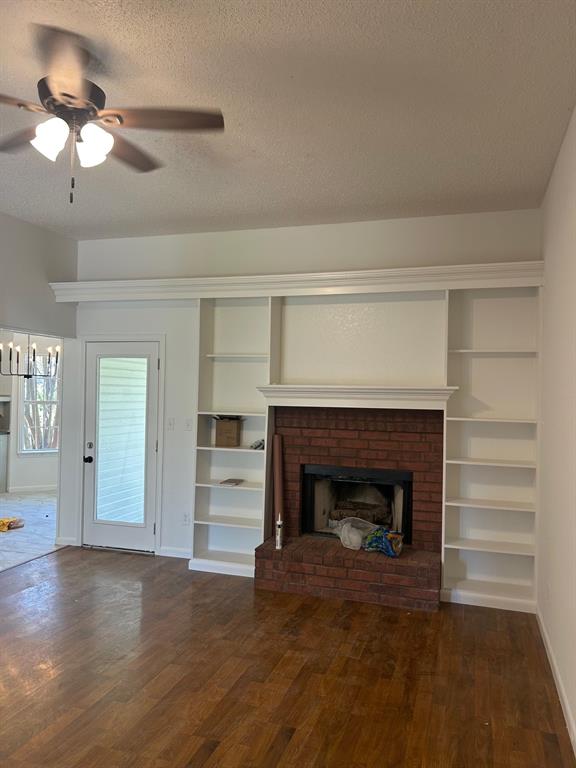 Brick fireplace with integrated shelving, crown molding, wood-finish flooring, and ceiling fan