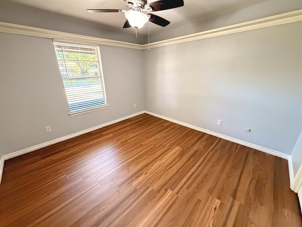 Room featuring wood-finish flooring, crown molding, a single window with horizontal blinds, and a ceiling fan with integrated lighting