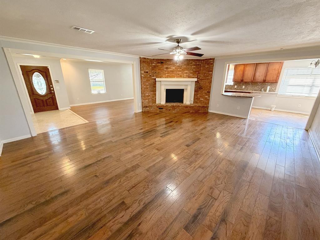 Corner brick fireplace with a white mantel, wood-finish flooring, and ceiling fan with integrated lighting