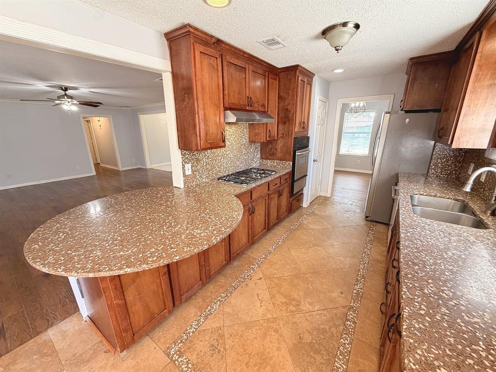 Kitchen featuring stained wood cabinetry, stone-composite countertops with a rounded breakfast bar, built-in stainless steel double wall oven, gas cooktop, and stone tile flooring