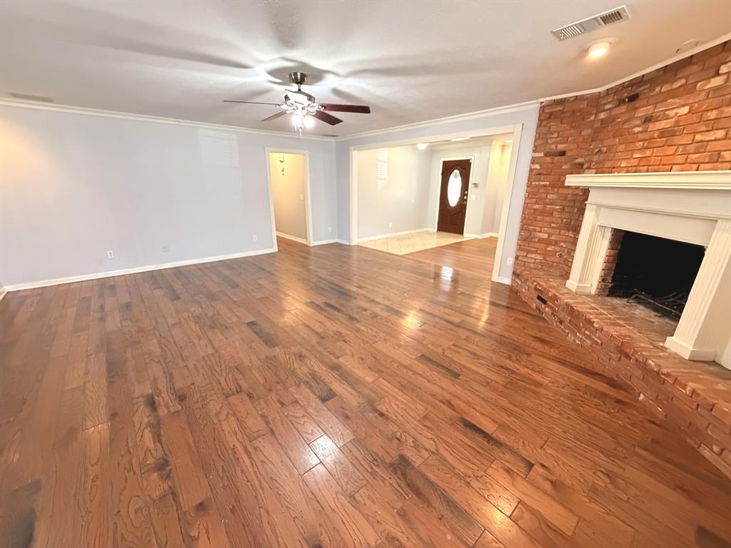Living area featuring wood-finish flooring, a floor-to-ceiling brick fireplace with a decorative mantel, and a ceiling fan with integrated lighting