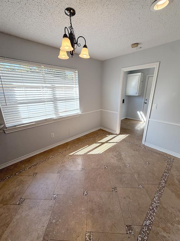 Interior space featuring large-format tile flooring with decorative stone-accented borders, white wainscoting, a three-light chandelier, and horizontal window blinds