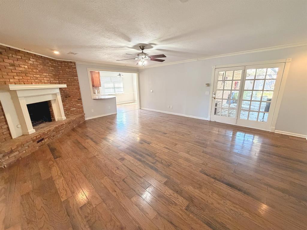 Living area featuring wood-finish flooring, a red brick fireplace with a white mantel, and glass-paned French doors