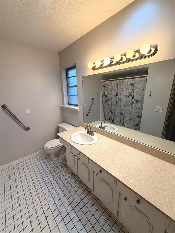 Bathroom featuring a large vanity with a neutral-tone countertop, an integrated sink, an expansive wall-mounted mirror, and tile flooring