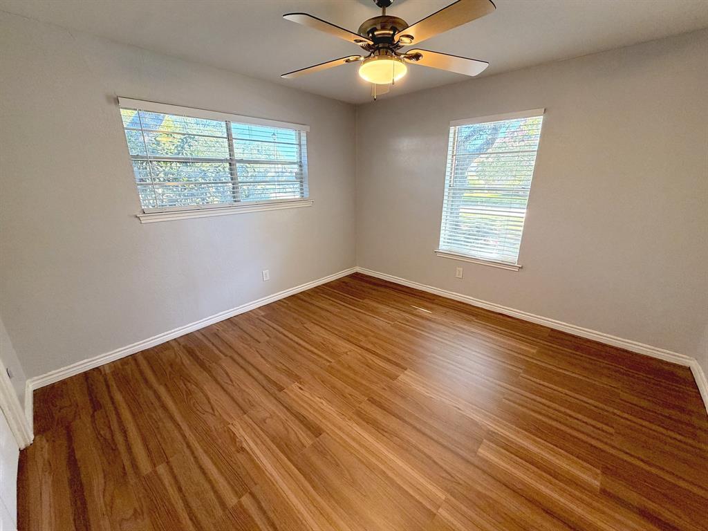 Room featuring wood-finish flooring, dual windows with horizontal blinds, and a central ceiling fan with integrated lighting