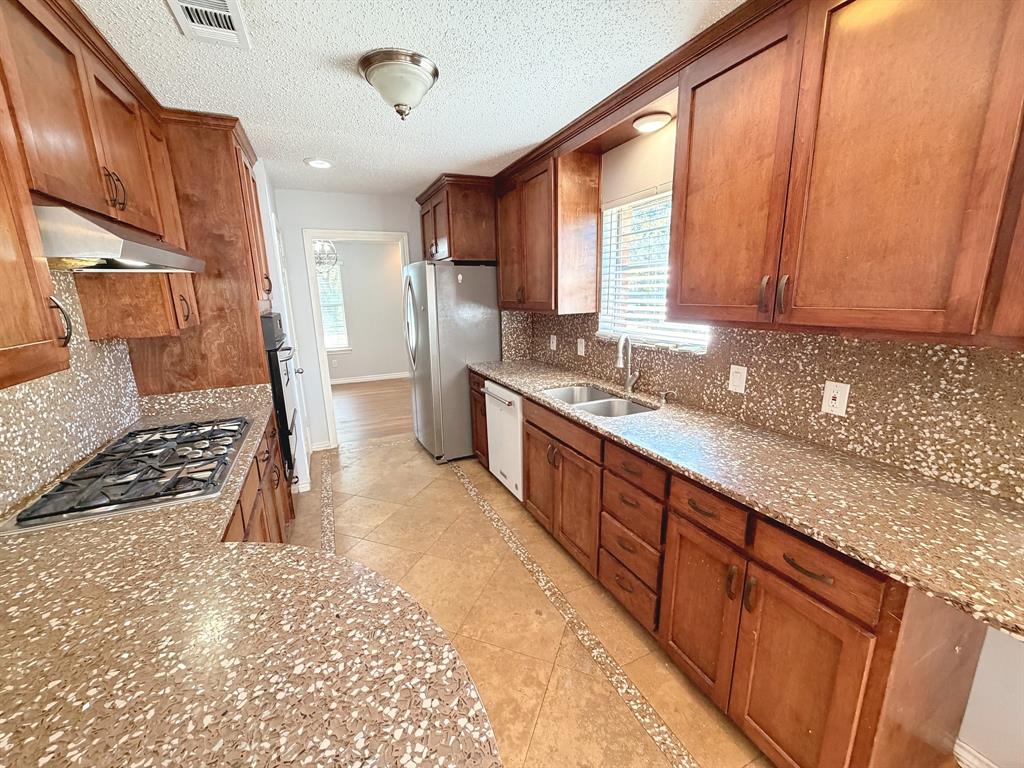Kitchen featuring stained wood cabinetry, stone-style countertops, mosaic tile backsplash, integrated stainless steel gas cooktop, and tile flooring