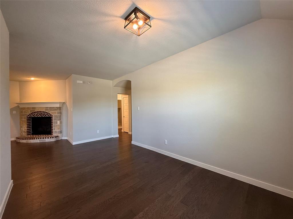 Living area featuring wood-finish flooring, vaulted ceilings, a geometric metal-frame light fixture, and a stone-surround corner fireplace with brick detailing