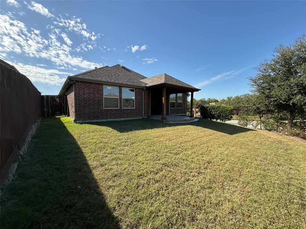 Brick exterior with a covered rear patio, shingled hip roof, and wood fencing Brick exterior with a covered rear patio, shingled hip roof, and wood fencing