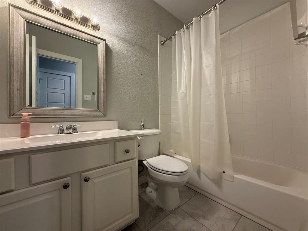 Bathroom featuring a white vanity cabinet with an integrated countertop, framed wall mirror, multi-bulb overhead lighting, and a bathtub with tile surround