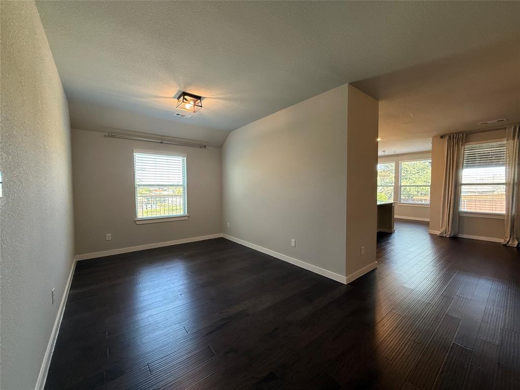 Spacious interior featuring dark wood-finish flooring, neutral wall paint, geometric flush-mount lighting, and large windows with horizontal blinds