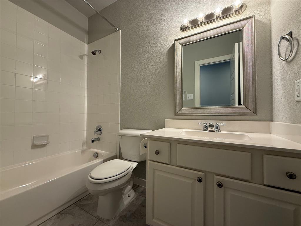 Bathroom featuring a white vanity cabinet with an integrated sink, framed wall mirror, multi-bulb vanity light, and a tile-surround shower and tub combination Bathroom featuring a white vanity cabinet with an integrated sink, framed wall mirror, multi-bulb vanity light, and a tile-surround shower and tub combination