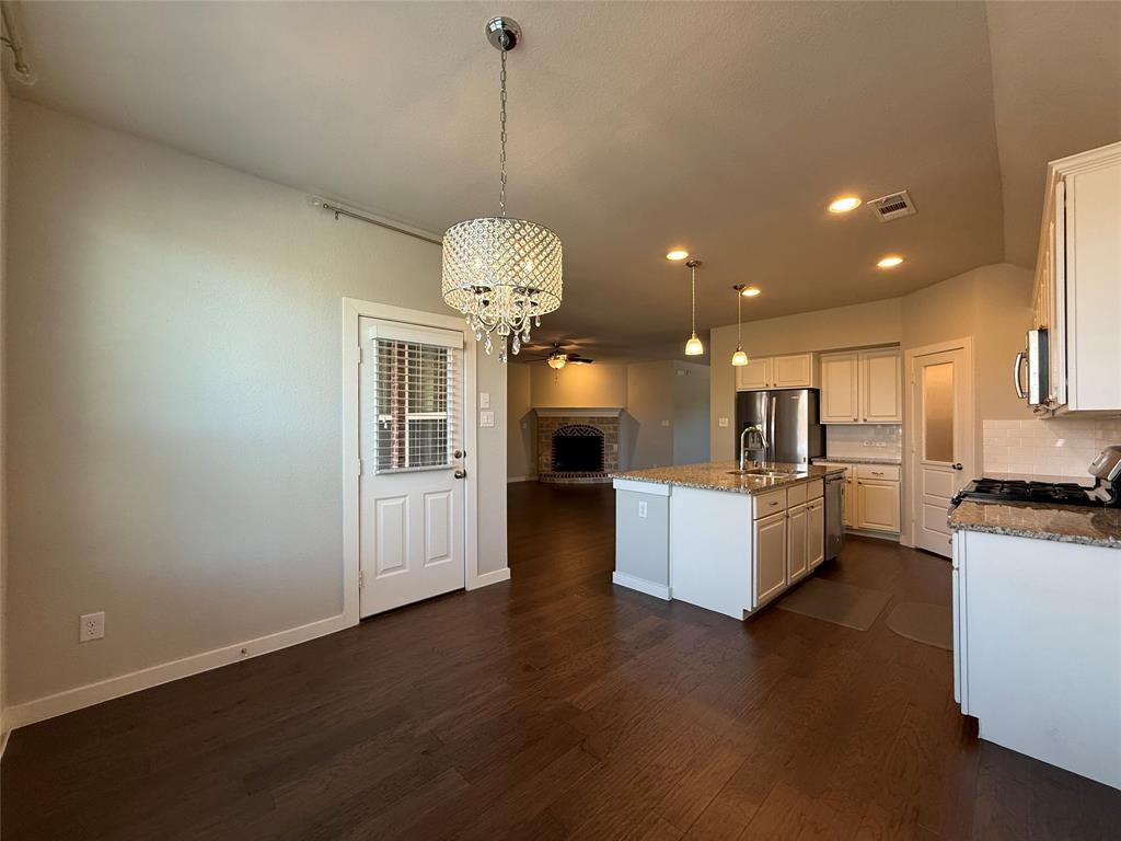 Kitchen featuring white cabinetry, stone countertops, stainless steel appliances, a center island with a built-in sink, and wood-finish flooring