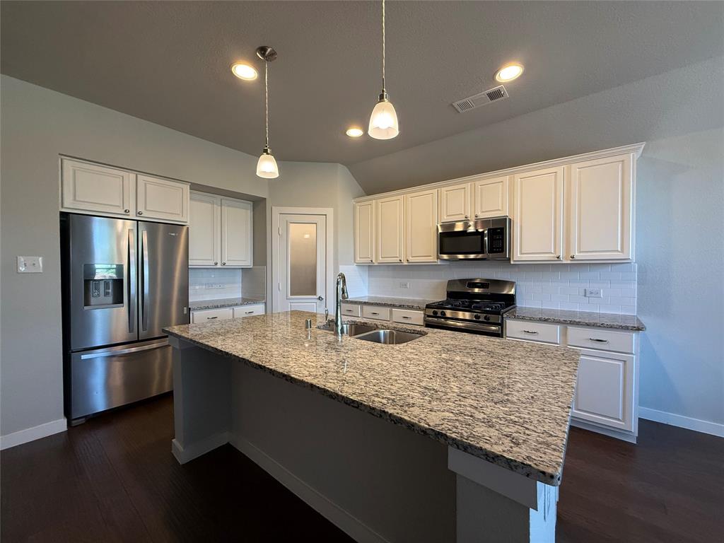 Kitchen featuring stone countertops, white cabinetry, stainless steel appliances, a central island with an integrated sink, and pendant lighting