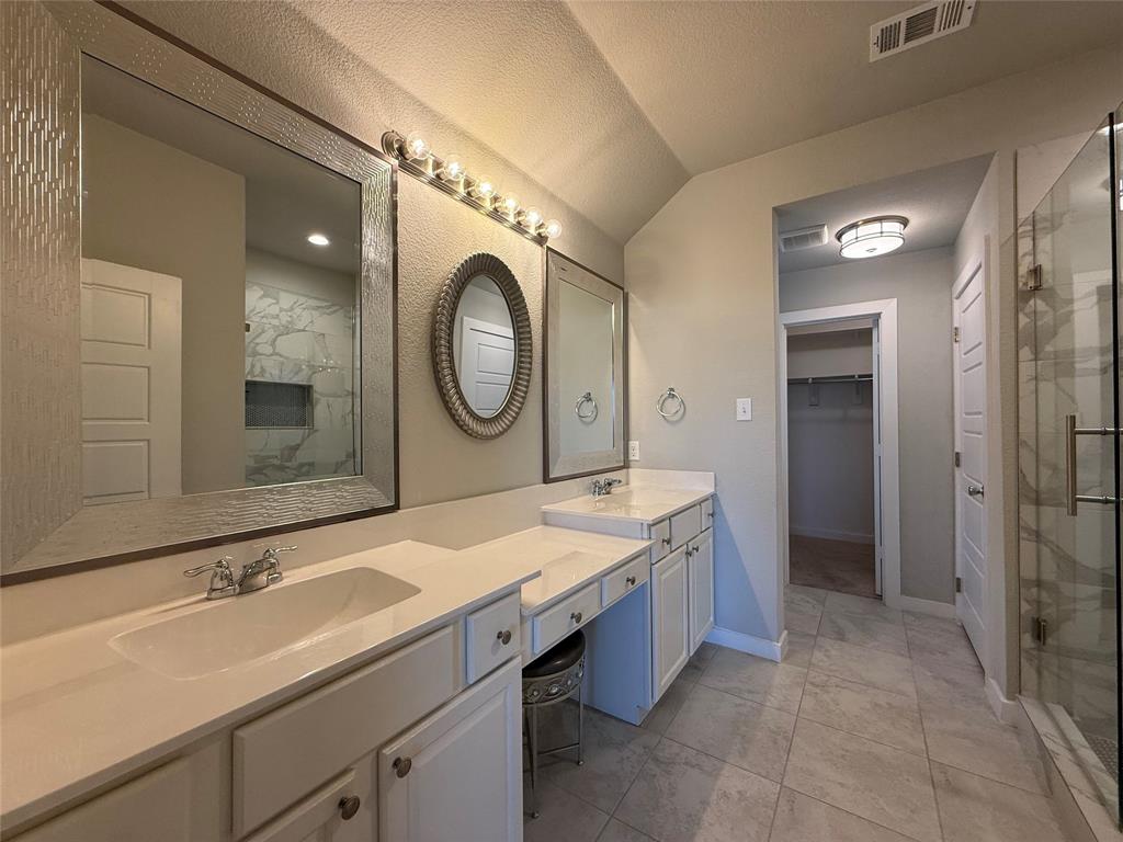 Dual-sink vanity with light-tone solid surface countertops, extensive wall-mounted mirrors, large-format tile flooring, and a glass-enclosed shower