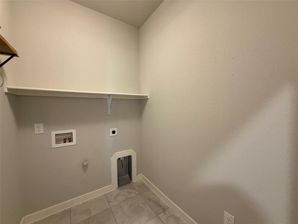 Utility space featuring tile flooring, neutral wall paint, and a mounted upper storage shelf