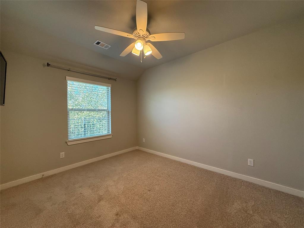 Neutral-toned room featuring a vaulted ceiling, neutral wall-to-wall carpeting, and a multi-blade ceiling fan with an integrated light fixture Neutral-toned room featuring a vaulted ceiling, neutral wall-to-wall carpeting, and a multi-blade ceiling fan with an integrated light fixture