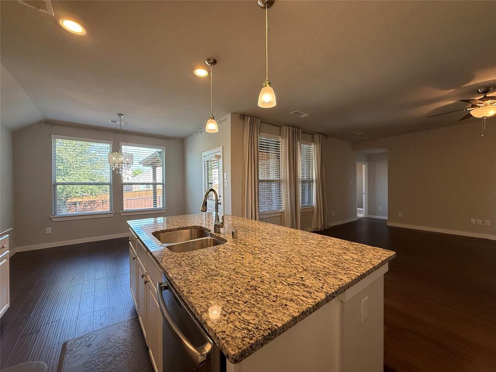 Kitchen island featuring stone countertops and an integrated dual-basin stainless steel sink, wood-finish flooring, recessed lighting, and pendant fixtures