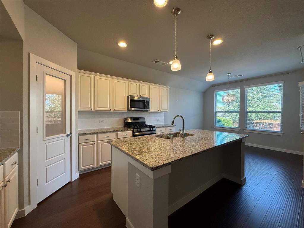 Kitchen featuring a central island with stone-finish countertops, shaker-style cabinetry, wood-finish flooring, glass-panel pantry door, and pendant lighting