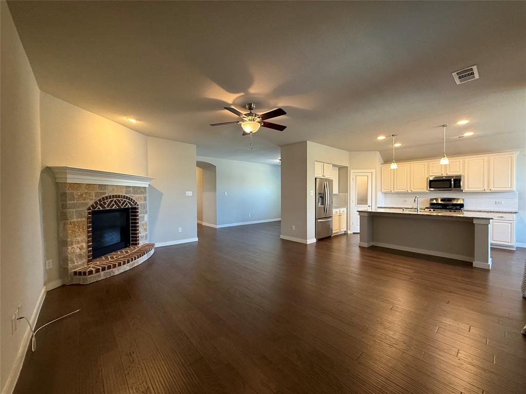 Open-concept interior featuring wood-finish flooring, a stone-surround fireplace with a brick-accented hearth, a kitchen island with stone countertops, and recessed lighting