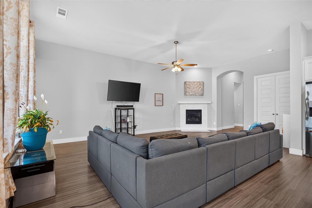 Living area featuring wood-finish flooring, vaulted ceilings, a fireplace with a white tile surround, a brushed metal ceiling fan, and arched architectural detailing