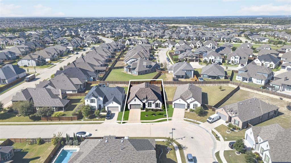Aerial perspective featuring a multi-gabled roofline, brick and stone exterior, paved driveway, and perimeter wood fencing
