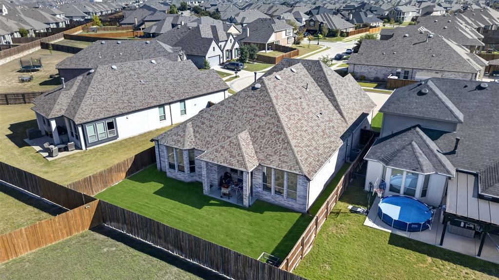 Aerial view of residential property featuring a brick and stone exterior, a rear-covered patio, and a fully fenced backyard with a grass lawn