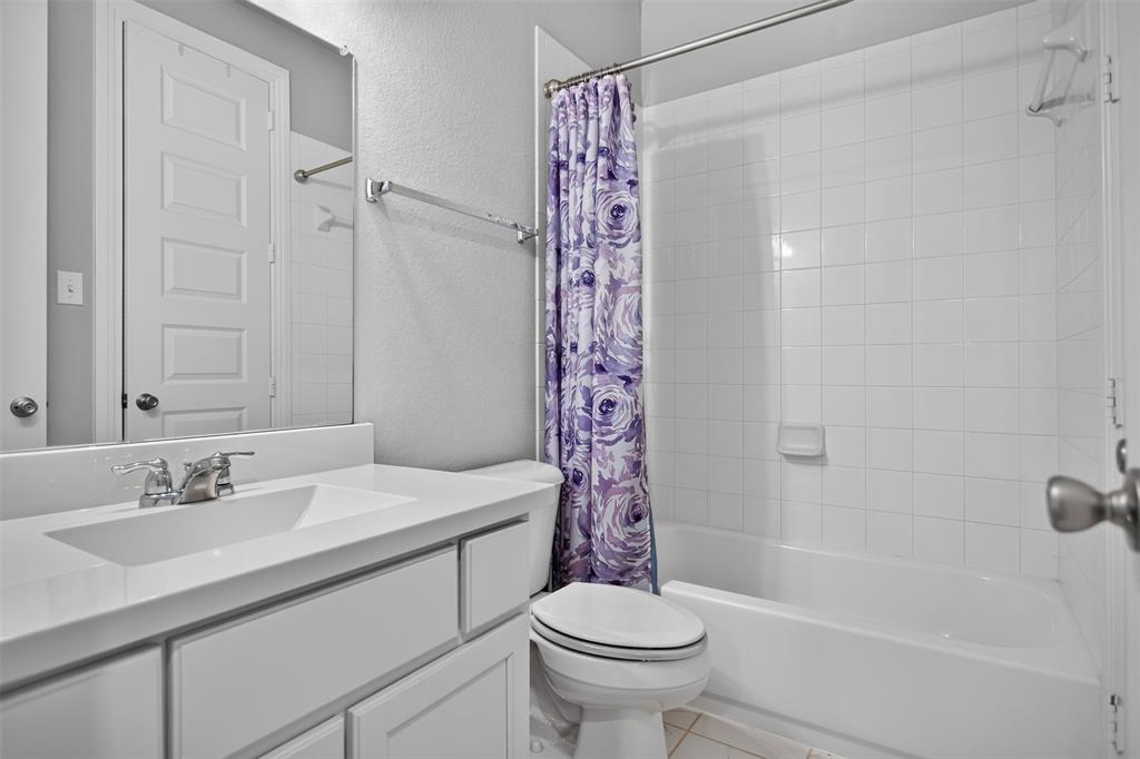 Bathroom featuring a white vanity cabinet, solid-surface countertop with an integrated sink, polished chrome faucet, and a shower-tub combination with white wall tile