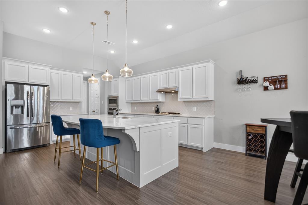 Kitchen featuring white cabinetry, an expansive island with a light-toned stone countertop, stainless steel refrigerator and built-in microwave, wood-finish flooring, and recessed lighting