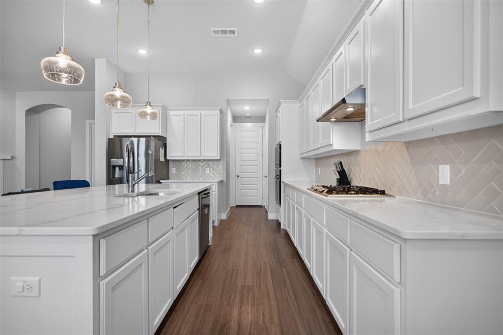 Kitchen featuring white shaker-style cabinetry, quartz countertops, a neutral herringbone-pattern backsplash, three glass pendant lights, and wood-finish flooring