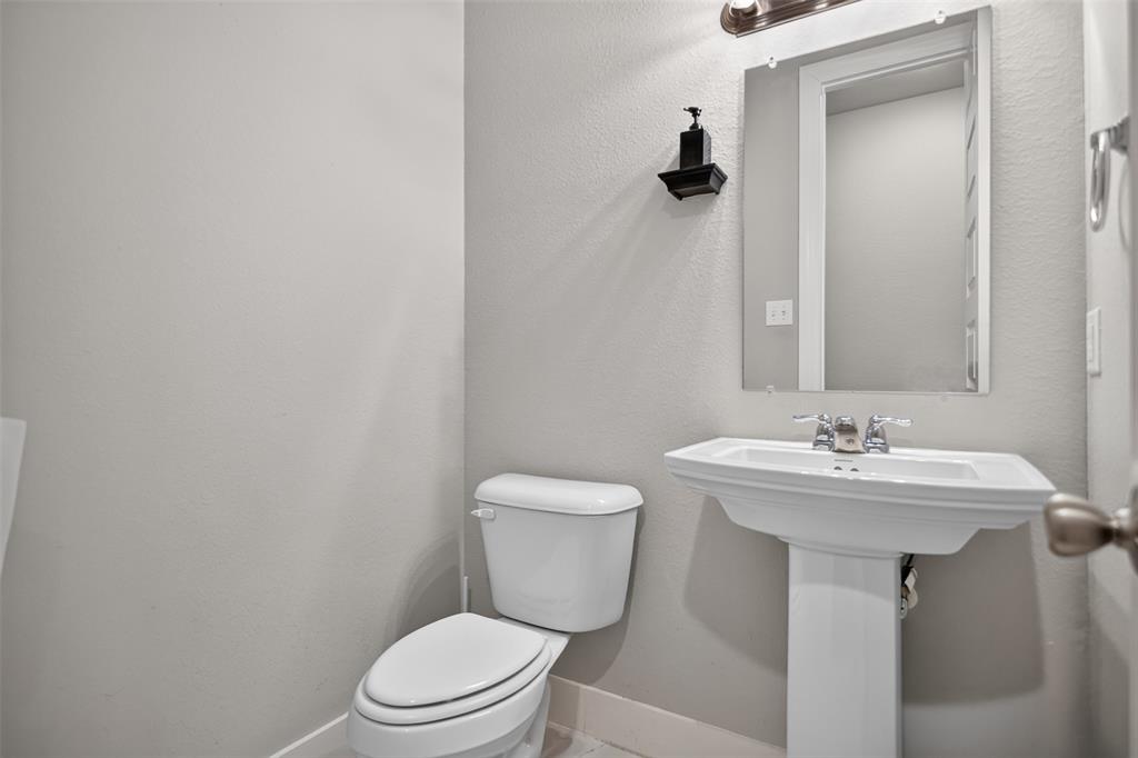 Bathroom featuring a white porcelain pedestal sink with a chrome dual-handle faucet, a wall-mounted rectangular mirror, and a wall-mounted light fixture