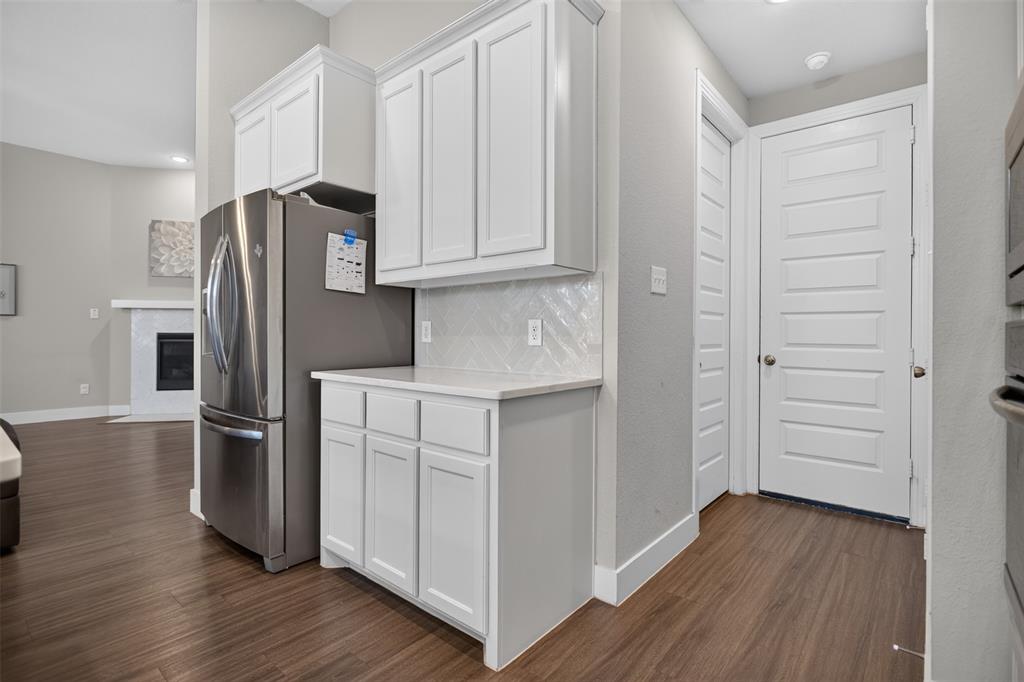 Kitchen area featuring white shaker-style cabinetry, herringbone-patterned tile backsplash, stone-surface countertop, stainless steel refrigerator, and wood-finish flooring
