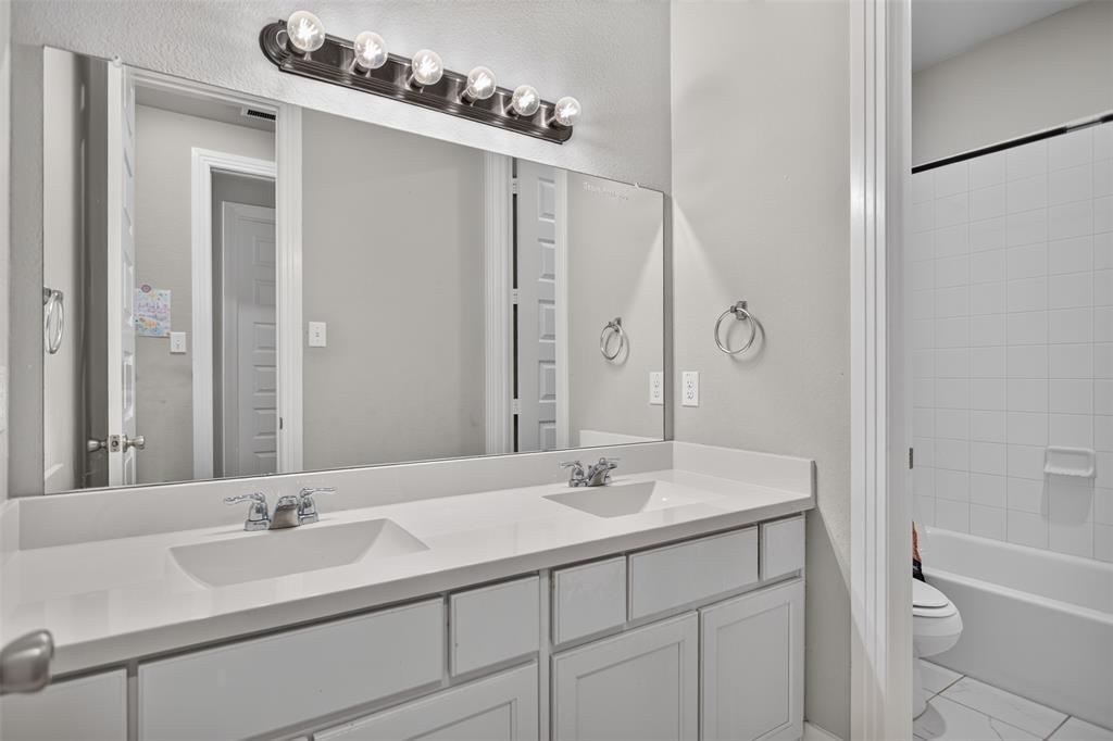 Double vanity featuring solid-surface countertops, dual integrated sinks, an expansive wall-to-wall mirror, and overhead multi-light fixture