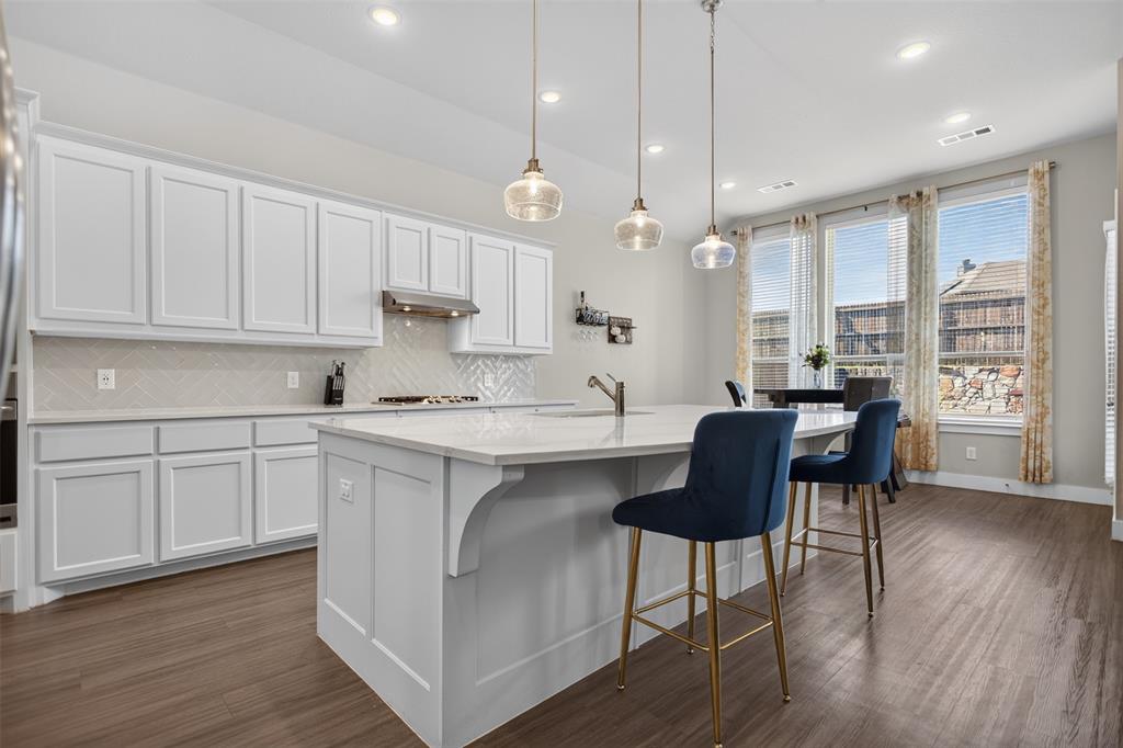Kitchen featuring white shaker-style cabinetry, a central island with countertop seating, herringbone-patterned tile backsplash, pendant lighting, and wood-finish flooring