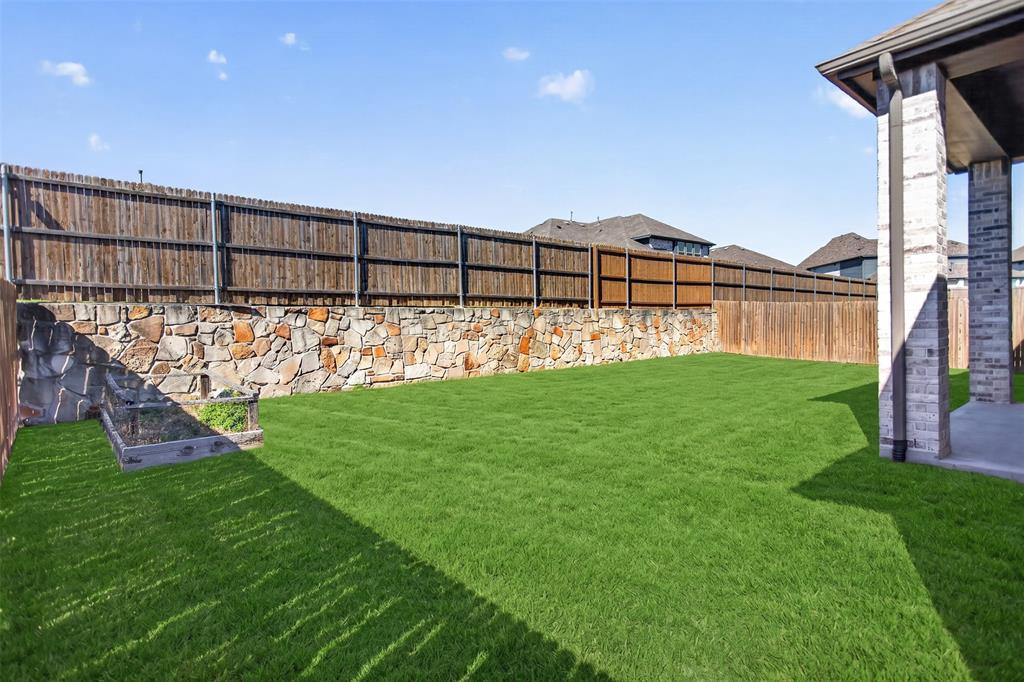 Backyard featuring a covered concrete patio, stone retaining wall, wood privacy fencing, and a built-in raised garden bed