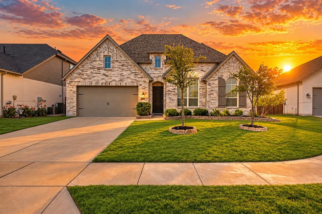 Multi-gabled brick and masonry exterior with an attached two-car garage, manicured lawn, and stone-bordered landscaping