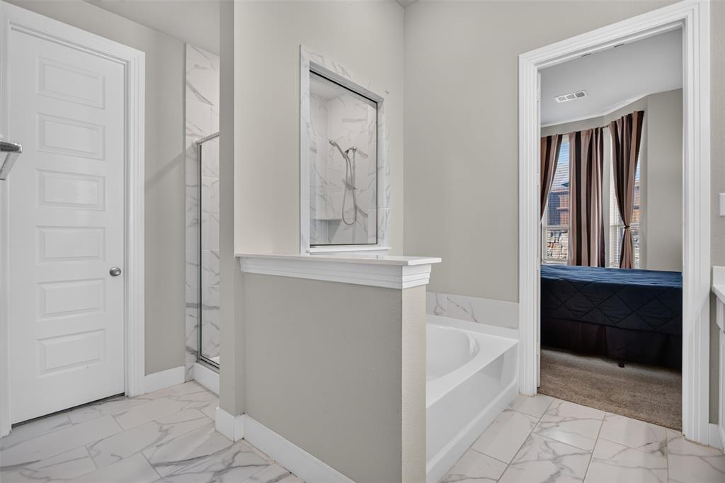 Bathroom featuring large-format tile flooring with marble-patterned finish, a built-in soaking tub, a separate shower enclosure with full-height tile surround, and a partial privacy wall