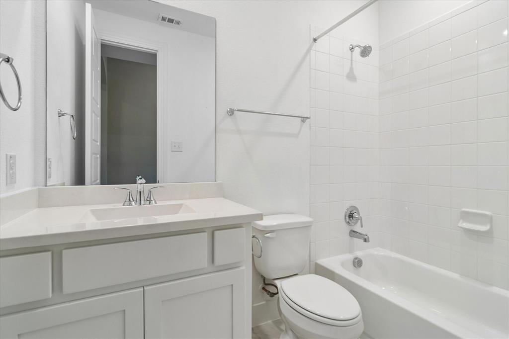 Bathroom featuring a white vanity with a composite countertop, an undermount sink, a full-width mirror, and a shower-tub combination with white wall tile