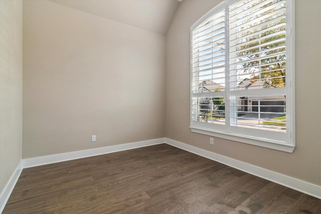 Room featuring a vaulted ceiling, wood-finish flooring, and a large arched window with integrated plantation shutters