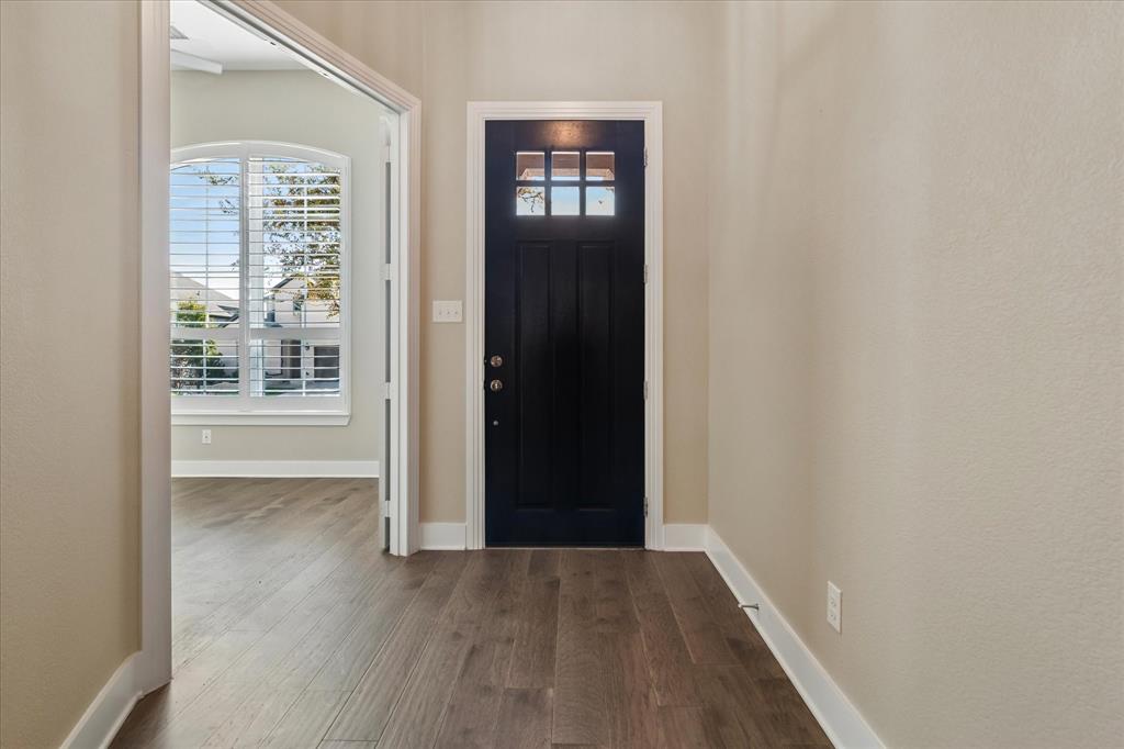 Entryway featuring a dark-toned door with a six-pane glass insert, wood-finish flooring, and arched window with plantation shutters
